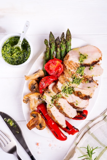 Grilled chicken breast on a plate with tomatoes, asparagus and mushrooms on a plate, flat lay