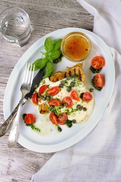 Grilled chicken breast topped with melted mozzarella cheese basil pesto tomato and caper