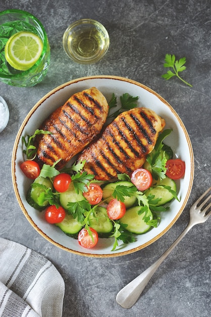 Grilled chicken breast with a salad of cherry tomatoes, cucumbers, arugula, and parsley