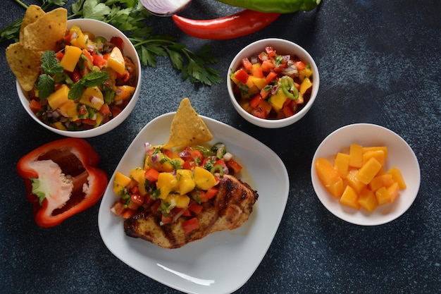 Grilled chicken breast with spicy salsa salad, mango, herbs, onions and peppers, corn chips. Mexican Food.