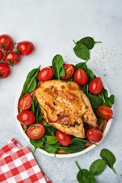 Grilled chicken breast with spinach green salad, pepper and cherry tomatoes in a ceramic plate at white table background. Healthy food, ketogenic diet, lunch concept. Top view and Copy space