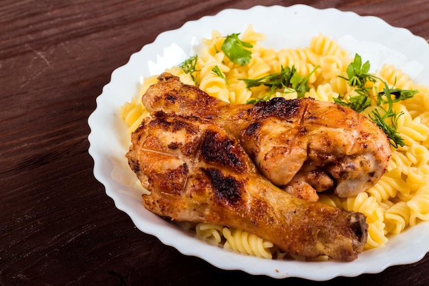 Grilled chicken drumstick and pasta on white plate brown wooden background