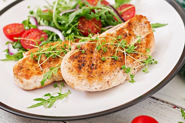 Foto filetto di pollo alla griglia e insalata di verdure fresche di pomodori, cipolla rossa e rucola.