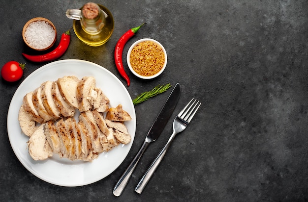 Grilled chicken fillet served in a white plate with spices on a stone background with copy space for your text.