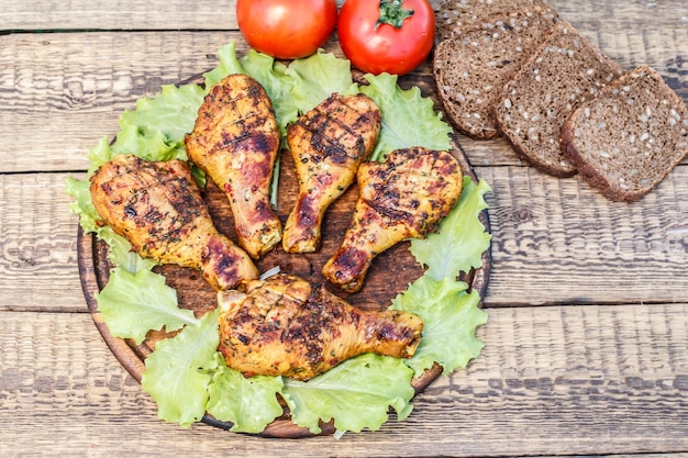 Grilled chicken legs and lettuce leaves on wooden cutting board fresh tomatoes and black bread