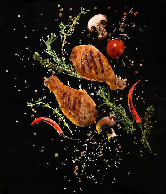 Grilled chicken legs with ingredients on black background
