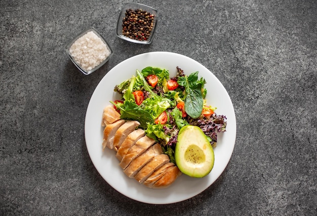 Foto carne di pollo alla griglia e insalata di verdure fresche di pomodoro, avocado, lattuga e spinaci