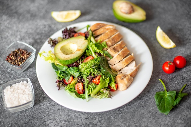 Carne di pollo alla griglia e insalata di verdure fresche di pomodoro, avocado, lattuga e spinaci