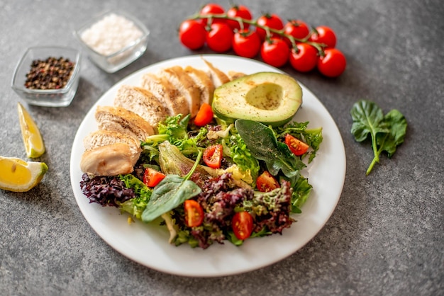 Carne di pollo alla griglia e insalata di verdure fresche di pomodoro, avocado, lattuga e spinaci