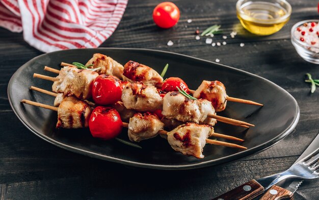 Spiedini di pollo alla griglia con pomodorini su un piatto nero. tavolo in legno nero. messa a fuoco selettiva