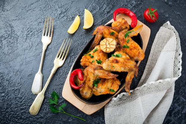 Grilled chicken wings on a cast iron pan on a black oval stone surface. Top view. Selective focus.