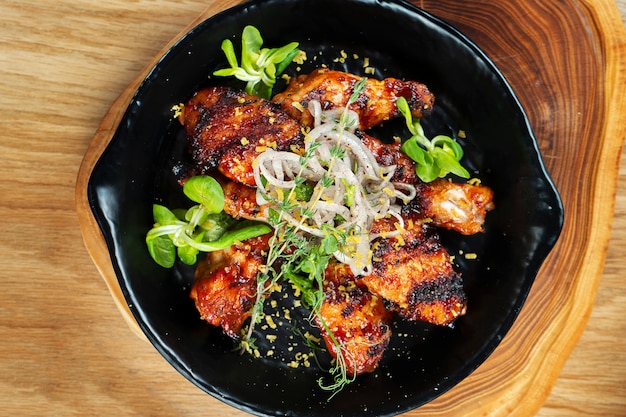 Grilled chicken wings in honey and beer sauce served in a decorative pan with herbs. Close up, selective focus. Wooden wall. Food photo