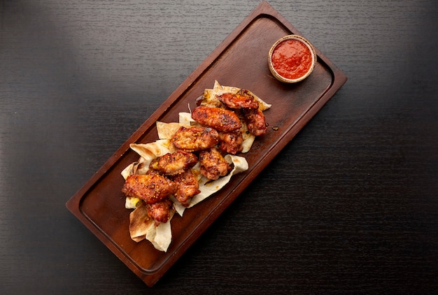 Grilled chicken wings in sauce, with ketchup, on a wooden board, on a dark background