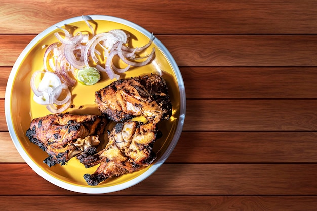 Grilled chicken wings with onion on a yellow plate on a wooden background