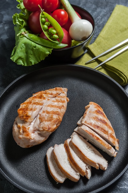 Grilled chiken fillet on frying pan and raw vegetables in bowl