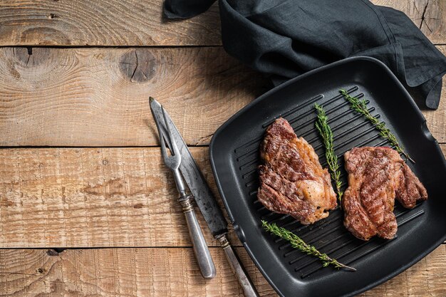 Grilled Chuck eye Roll beef steaks with herbs on grill skillet. Wooden background. Top view. Copy space.