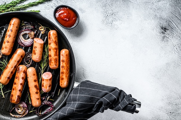 Grilled classic pork sausages with onion, garlic and rosemary in a pan. Black background. Top view. Copy space