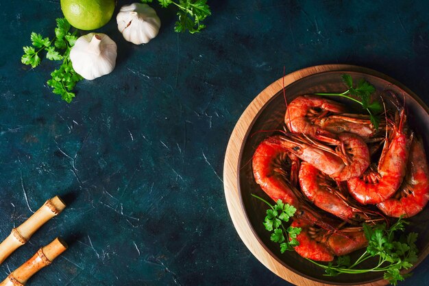 Grilled cooked argentine prawns, langoustines with herbs, garlic and lemon on a dark background, top view. High quality photo