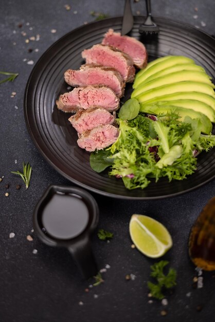 grilled cooked piece of tuna fillet with sliced avocado and salad on black ceramic plate