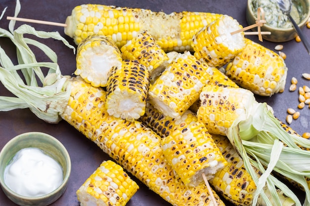 Grilled corn and bowls with sauce. Pieces of corn on skewers. Rusty metal background. Top view