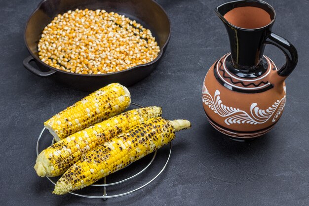 Grilled corn, corn pan and ceramic jug. Black background. Top view