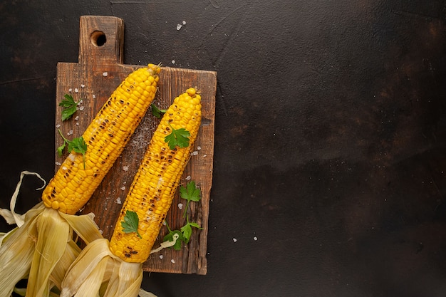 Grilled corn with greens and salt on the background of concrete