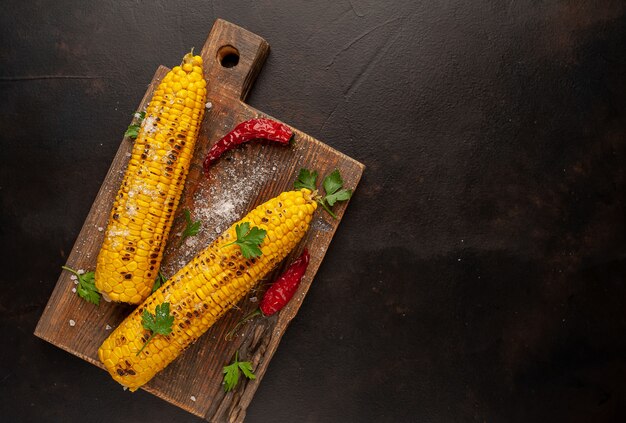 Grilled corn with greens and salt on the background of concrete