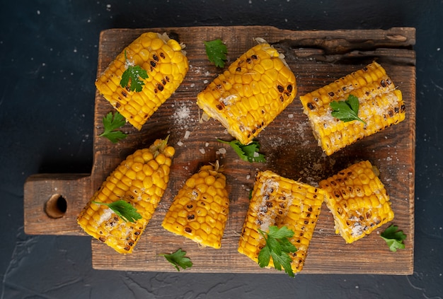 Photo grilled corn with greens and salt on the background of concrete