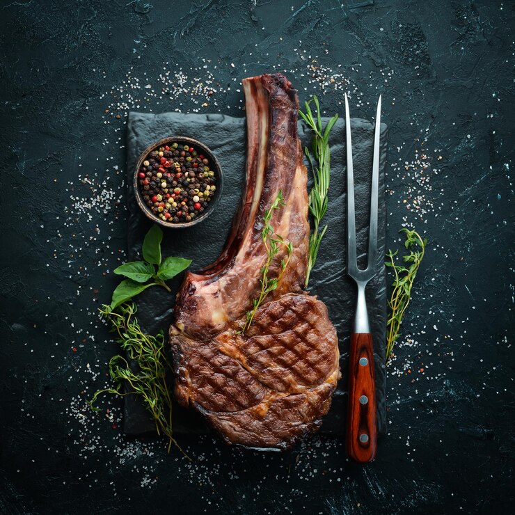 Grilled cowboy beef steak herbs and spices on a black stone background Barbecue Top view Free space for text
