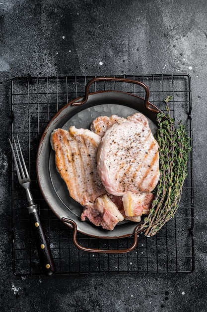 Grilled delicious pork chop steaks with herbs and spices Black background Top view