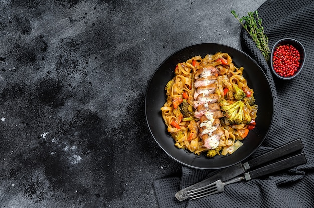 Grilled duck breast with Udon noodles and vegetables. Black background.