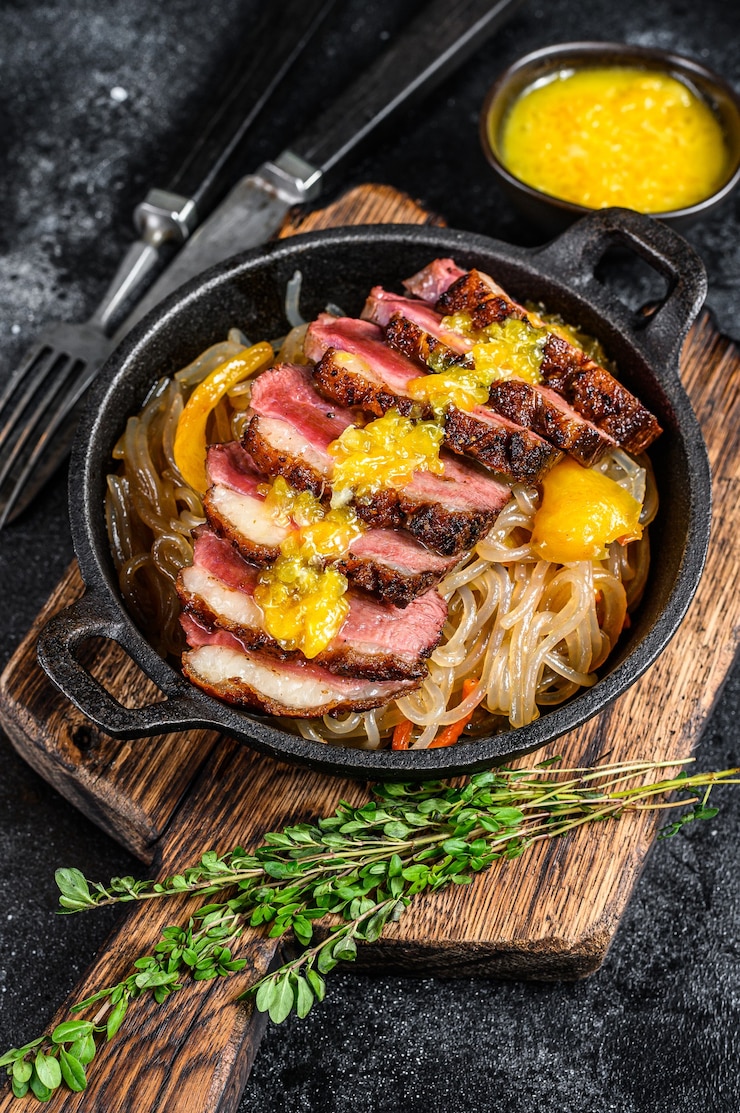 鴨肉の胸肉フィレステーキのグリル、麺とみかんソース添え。黒の背景。上面図。