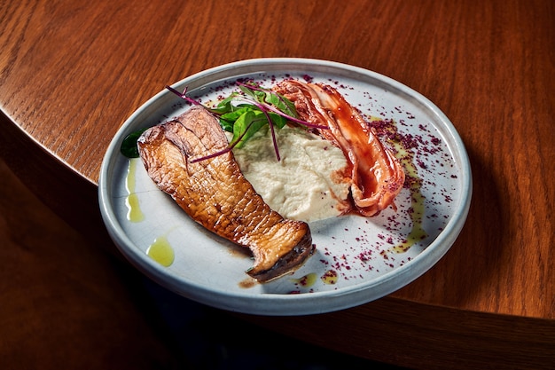 Grilled eryngii mushroom with kimchi cabbage and celery puree\
served in a white plate on a wooden table. restaurant food. close\
up view grilled slices of king oyster mushrooms