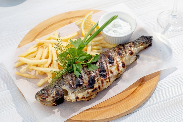 Pesce alla griglia guarnito con erbe e patatine fritte