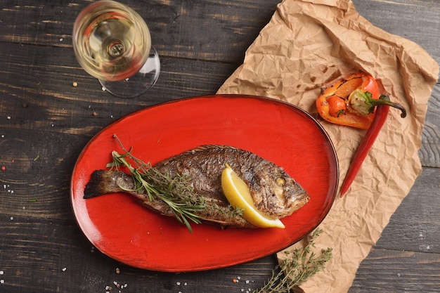 Grilled fish with lemon and a sprig of rosemary. In a red plate on a wooden table