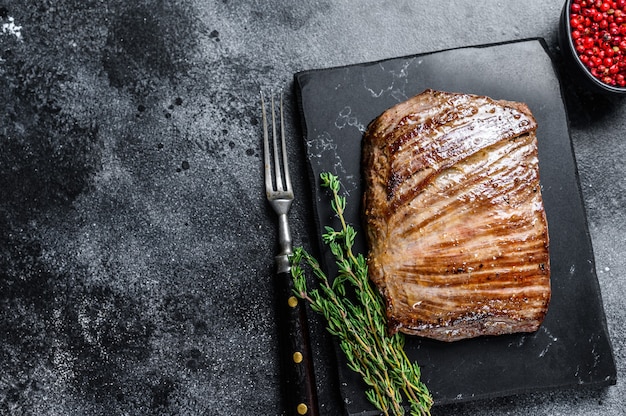 Grilled flank beef meat steak on a marble board. Black background. Top view. Copy space.