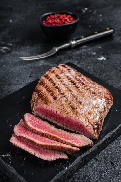 Grilled Flank Steak BBQ on a marble board Black background Top view