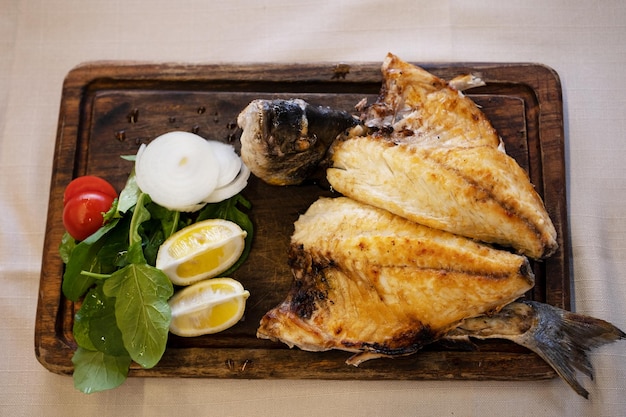 Grilled fried fish with vegetables and lemon on wooden cutting boardHigh angle top viewConcept of dish in restaurantsea foodtable layouthealthy and tasty eating