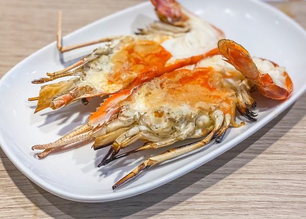 Grilled giant river prawn on white dish with spicy seafood sauce. Popular Thai food on wooden table as background