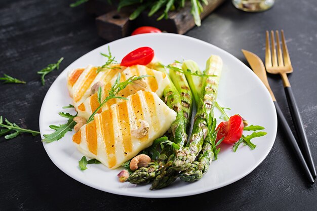 Insalata di formaggio halloumi alla griglia con pomodori e asparagi su piastra su sfondo scuro. cibo vegetariano sano.