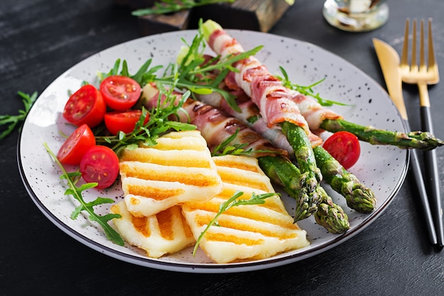 Insalata di formaggio halloumi alla griglia con pomodori e asparagi in strisce di pancetta sul piatto su sfondo scuro. cibo salutare.