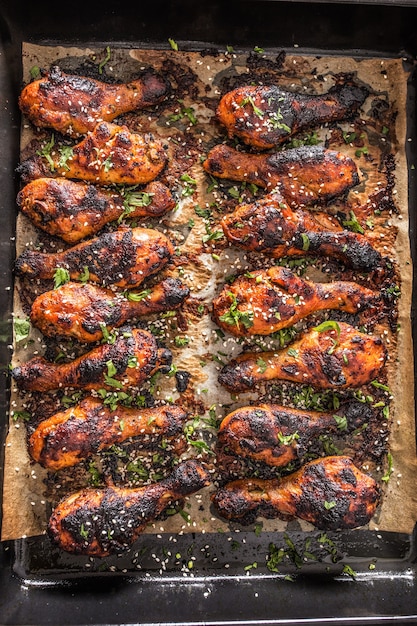 Foto cosce di hicken grigliate bbq con spezie, erbe aromatiche e sesamo su carta da forno - vista dall'alto. farina di pollame arrosto in teglia.