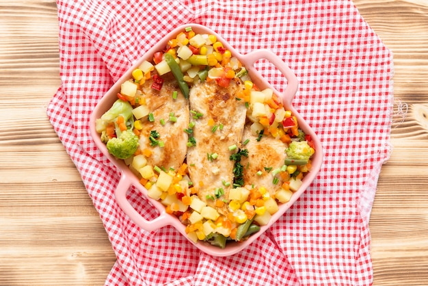 Grilled homemade chicken with various delicious vegetables on a light wooden background. Top view.