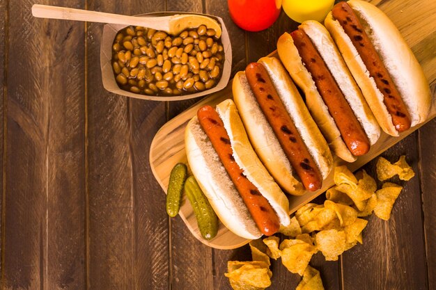 Grilled hot dogs on a white hot dog buns with chips and baked beans on the side.