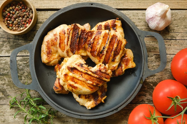 Photo grilled juicy chicken thigh fillets on an old wooden table with tomatoes garlic an rosemary closeup view from above