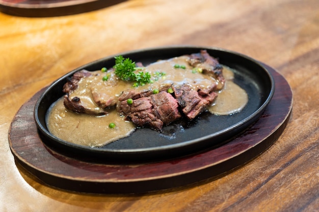 Grilled Juicy steak medium rare beef with herbs and spices on pan hot topped with black pepper sauce