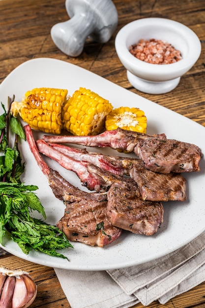 Grilled lamb chops steaks in a plate with corn and tomato. wooden background. Top view.