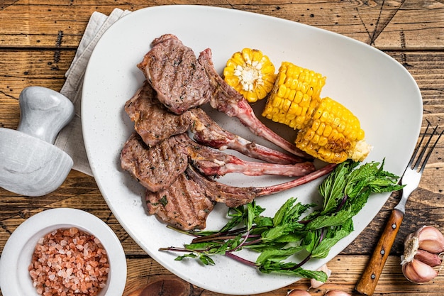 Grilled lamb chops steaks in a plate with corn and tomato. wooden background. Top view.