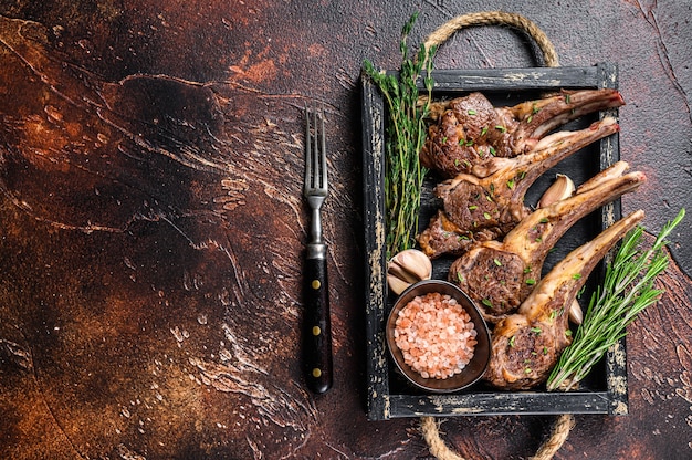 Bistecche di costolette di agnello alla griglia in un vassoio di legno. sfondo scuro. vista dall'alto. copia spazio.