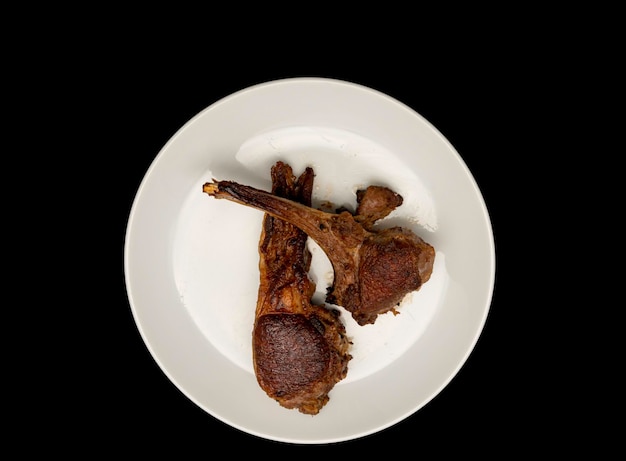 Grilled lamb chops on white plate isolated on black background Top view or flat lay